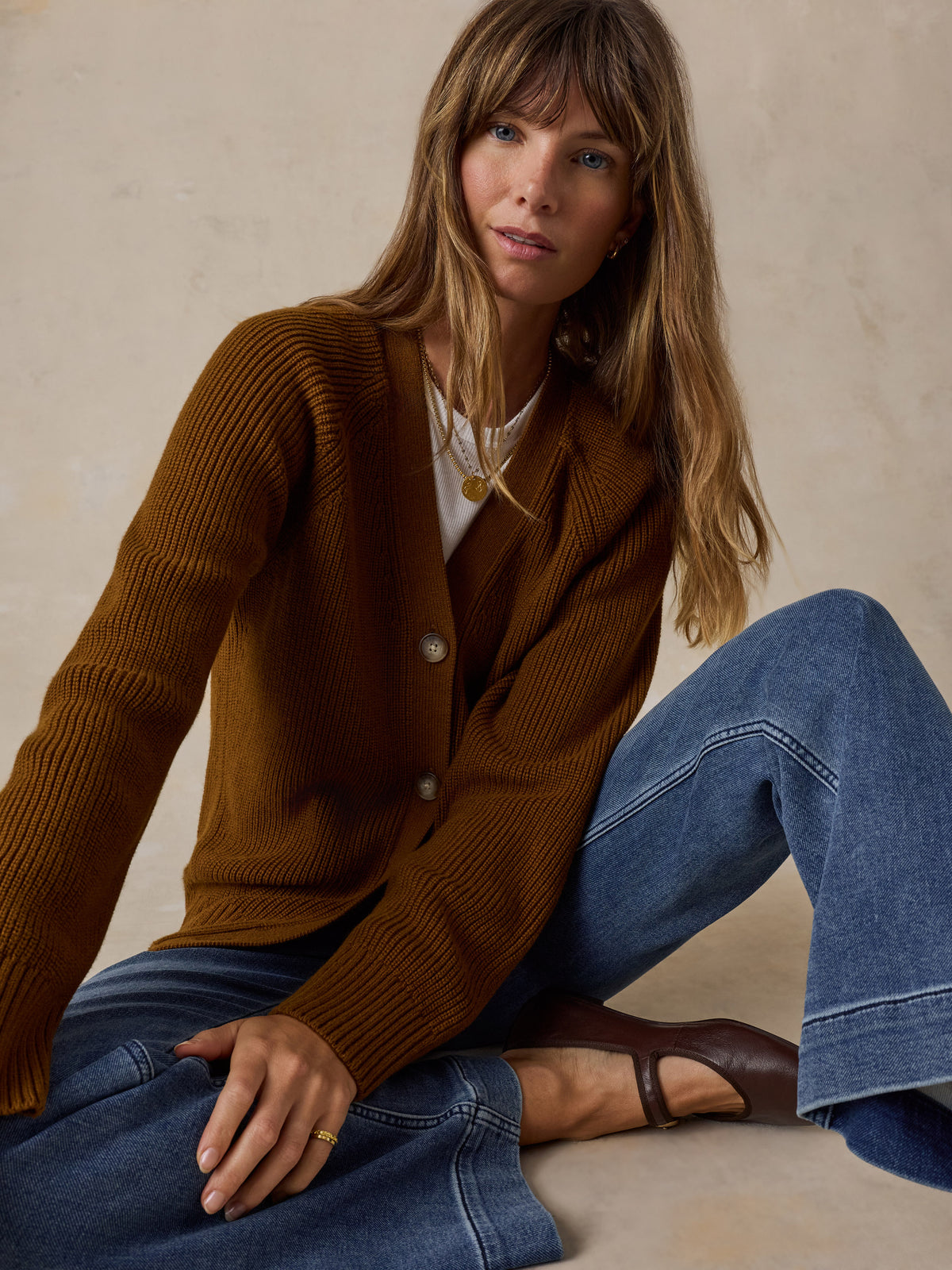 A woman wearing a ribbed brown cardigan over a white top and blue jeans, image 4 of 5