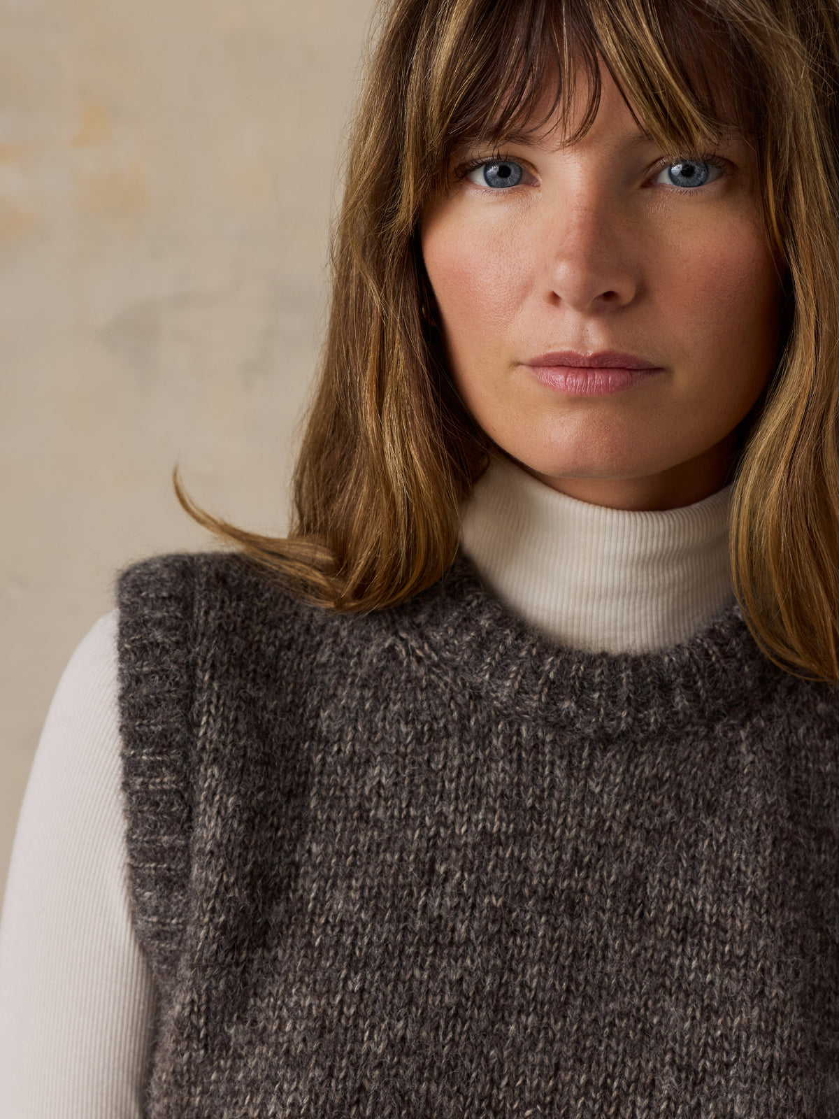 Close up of a woman wearing a grey sweater vest over a white turtleneck, image 5 of 5