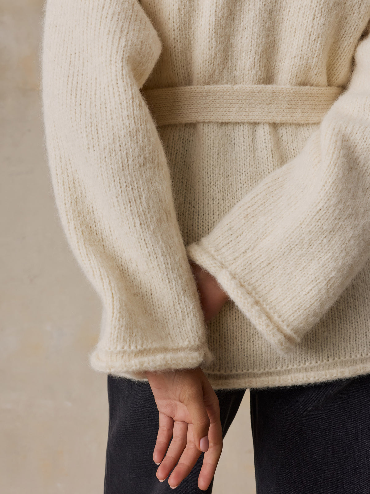 Close up of a woman wearing a cream wrap cardigan and black jeans, image 4 of 8