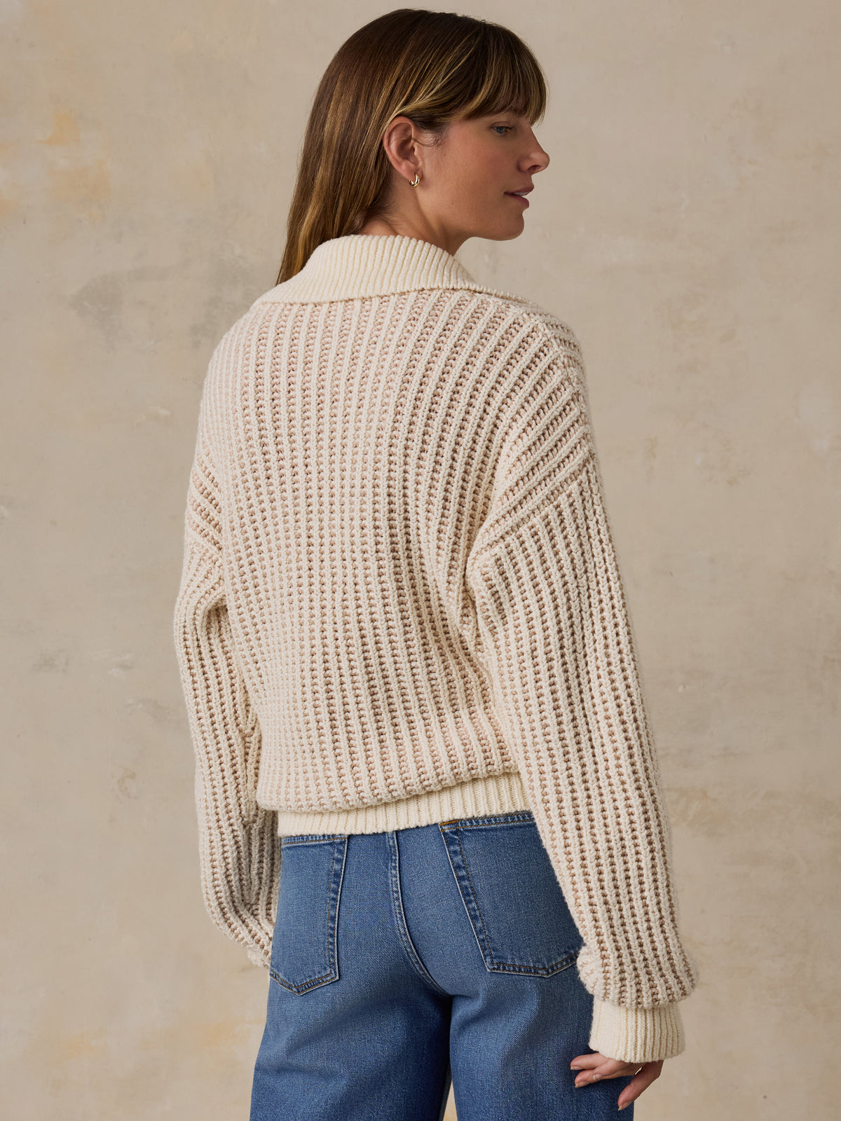 A woman wearing a cream-colored waffle-knit polo sweater and blue jeans, image 3 of 5
