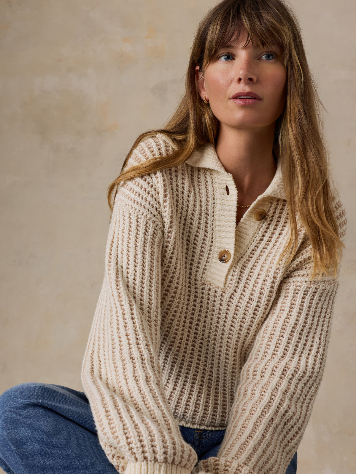 A woman wearing a cream-colored waffle-knit polo sweater and blue jeans, image 2 of 5