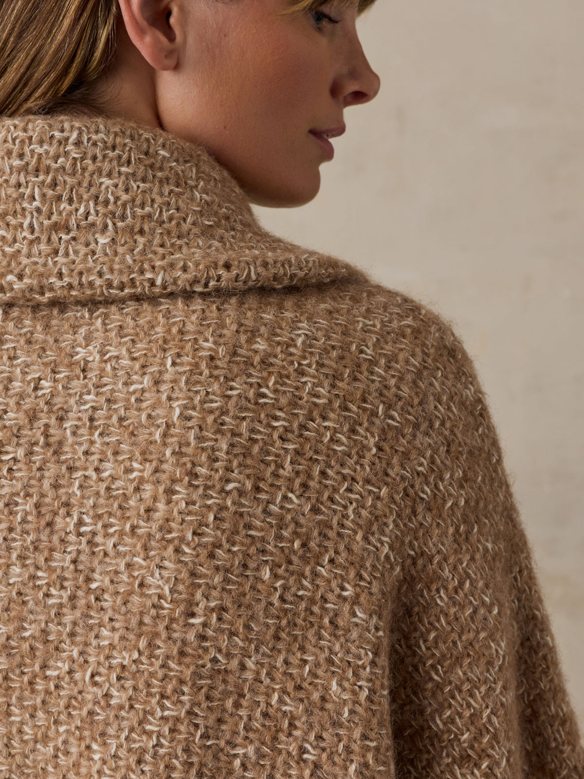 Close up of a woman wearing a beige sweater poncho, image 5 of 7