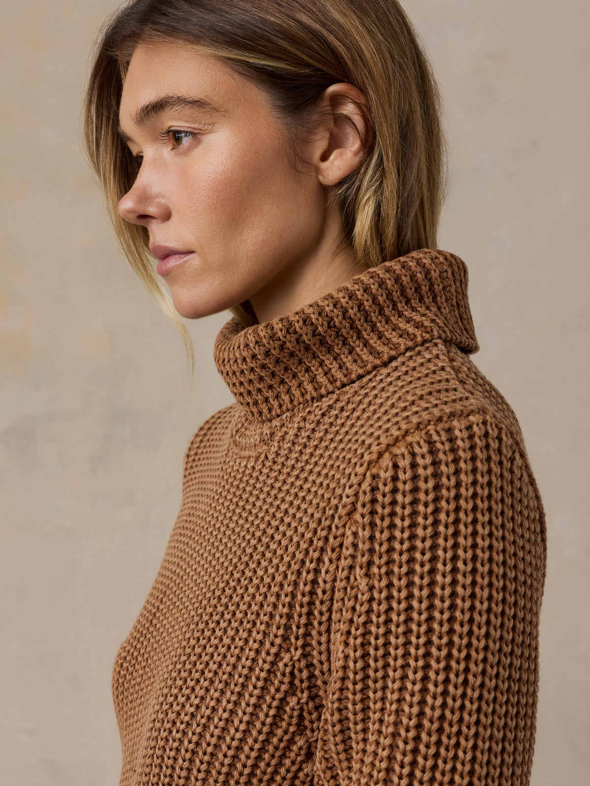 Woman wearing a brown knit turtleneck sweater against a beige studio background, image 4 of 7