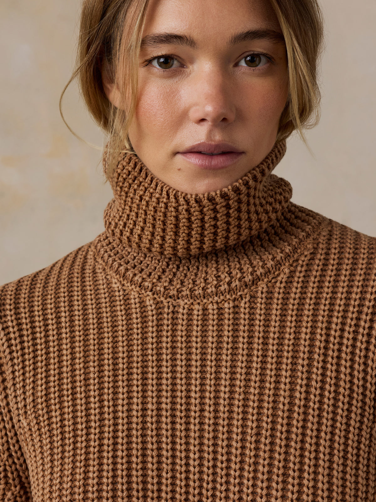 Woman wearing a brown knit turtleneck sweater against a beige studio background, image 6 of 7