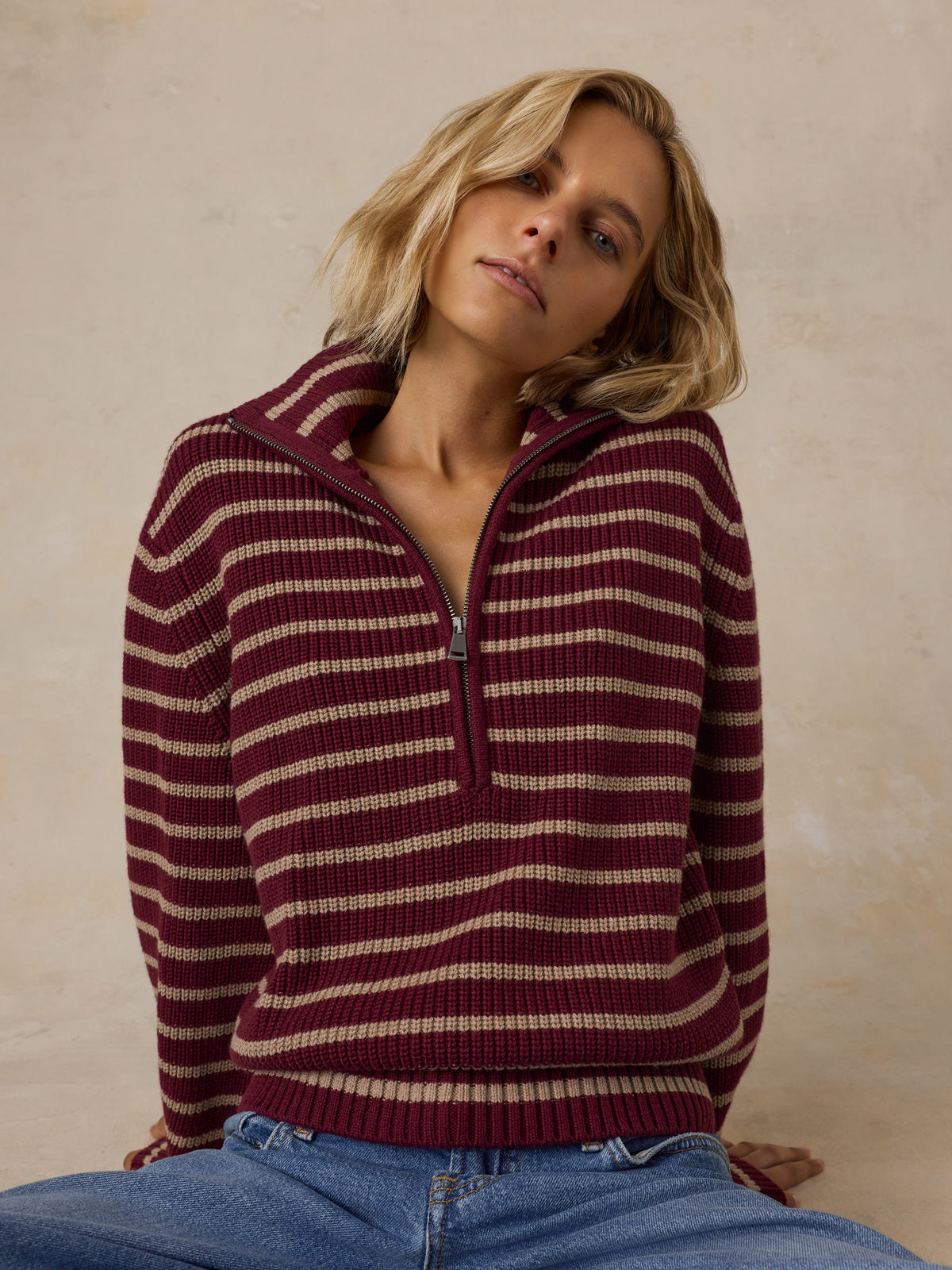 A woman wearing a burgundy and beige striped quarter-zip knit sweater with blue jeans, image 5 of 5