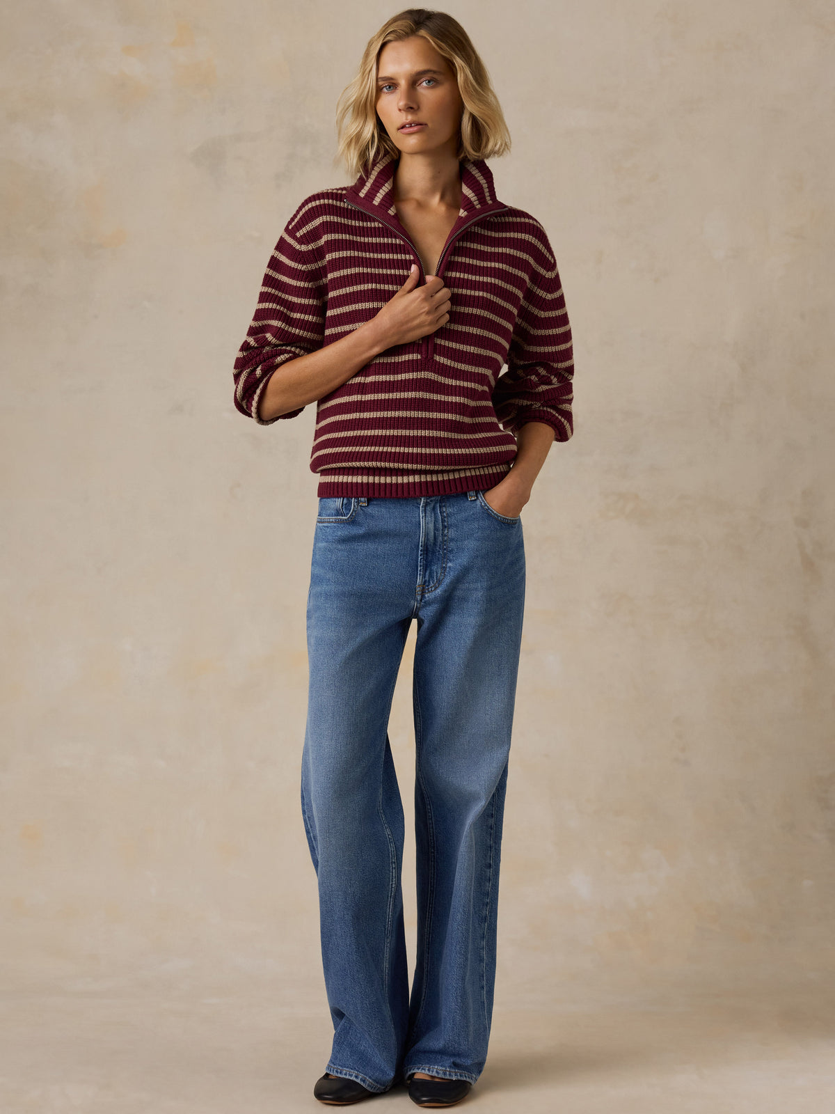 A woman wearing a burgundy and beige striped quarter-zip knit sweater with blue jeans, image 4 of 5