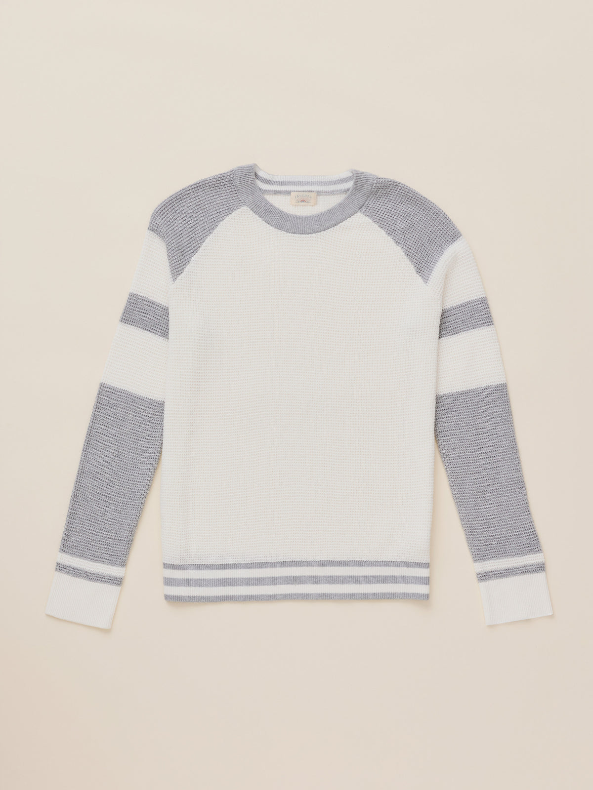 A long-sleeve knit sweater with a white body, gray shoulder yoke, and gray horizontal stripes on the sleeves and hem, displayed flat against a light beige background.