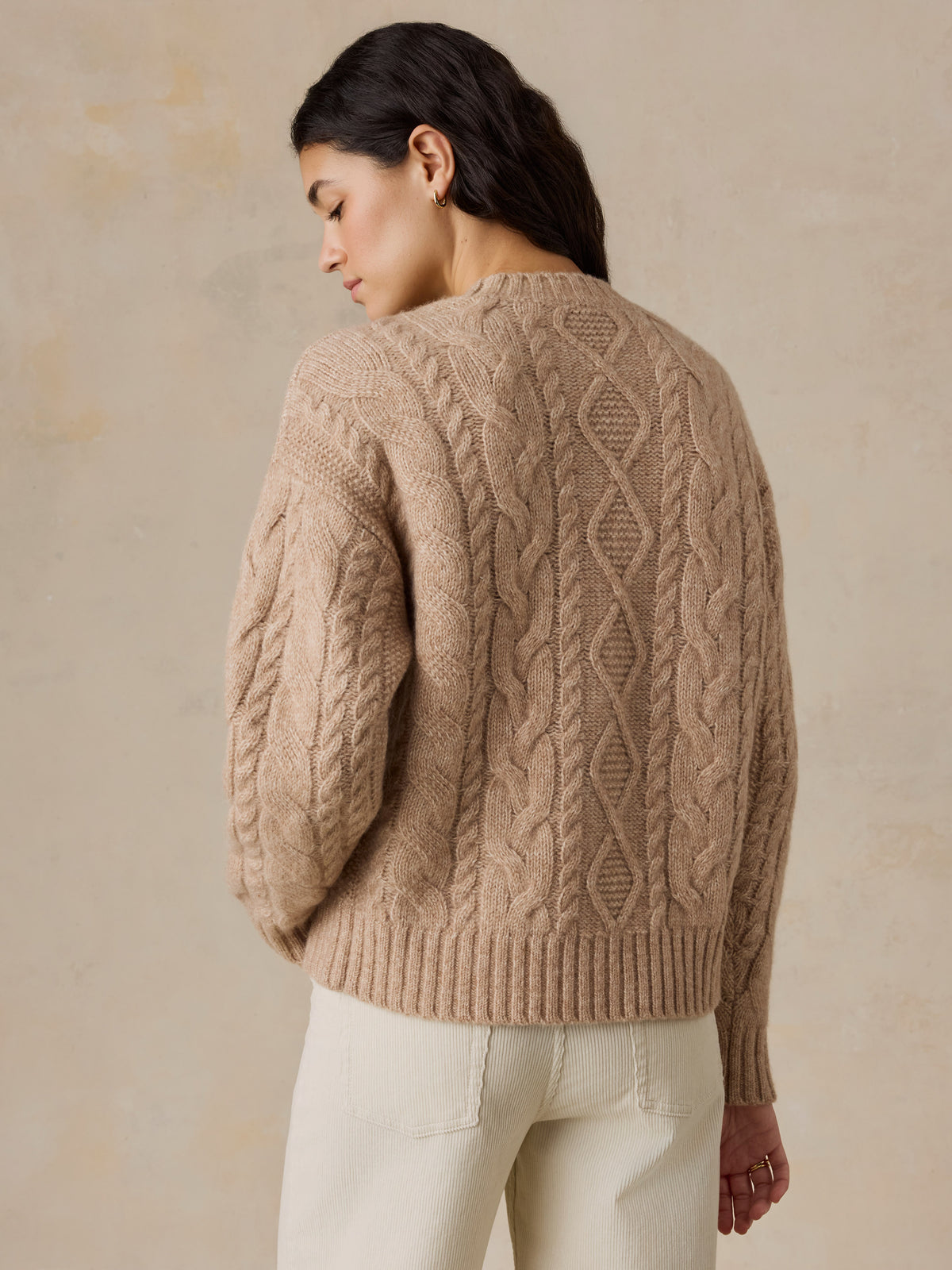 A woman viewed from behind wearing a beige sweater and white pants, image 5 of 5
