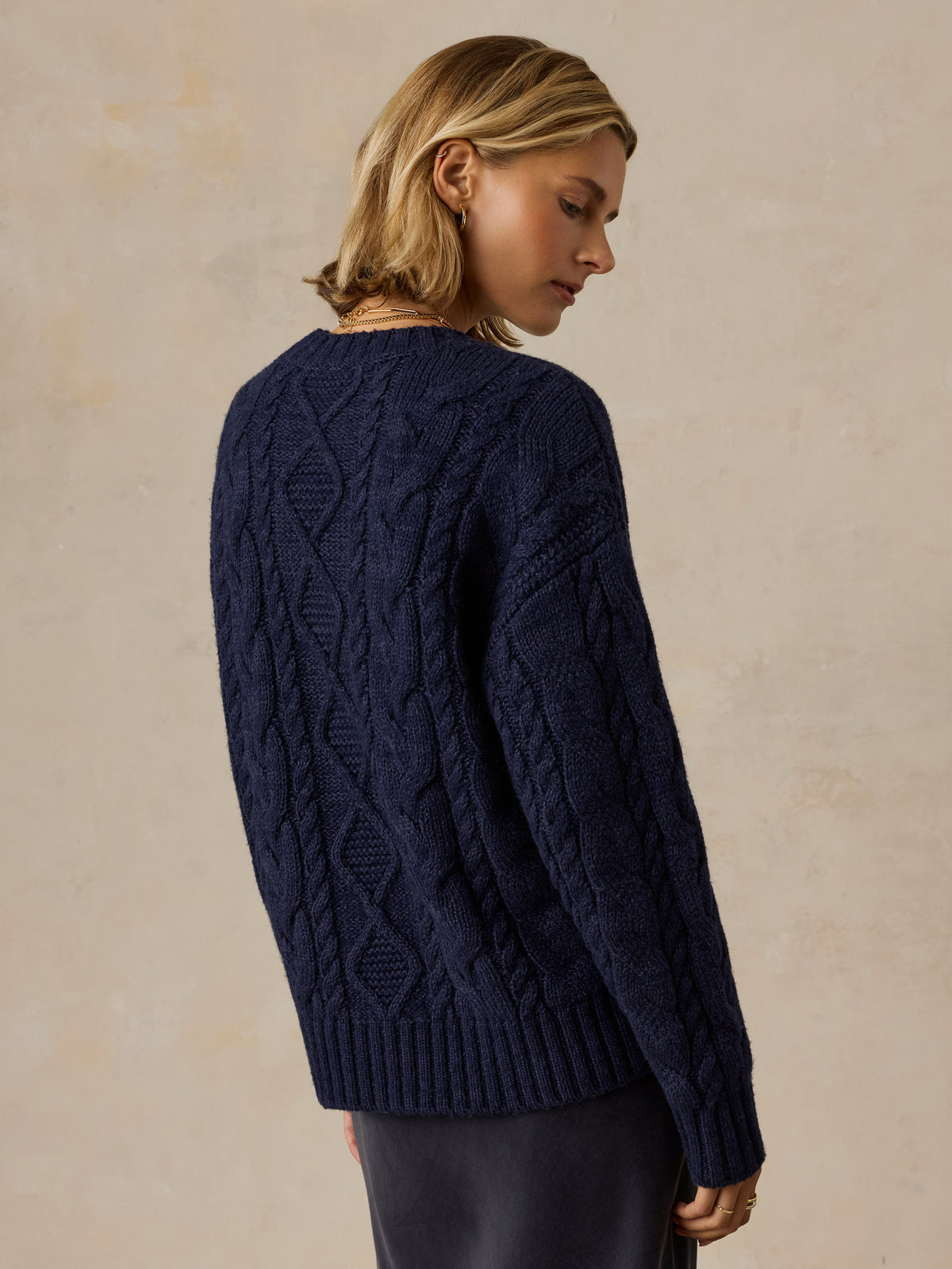 A woman viewed from behind wearing a blue sweater and black skirt, image 4 of 5