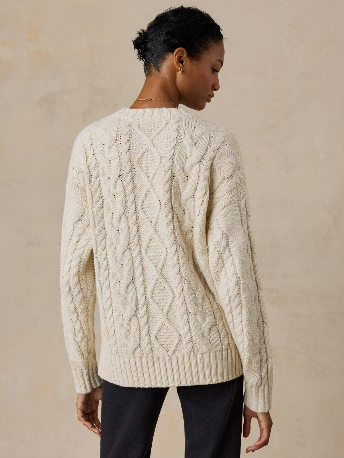 A woman viewed from behind wearing a white sweater and black jeans, image 3 of 5