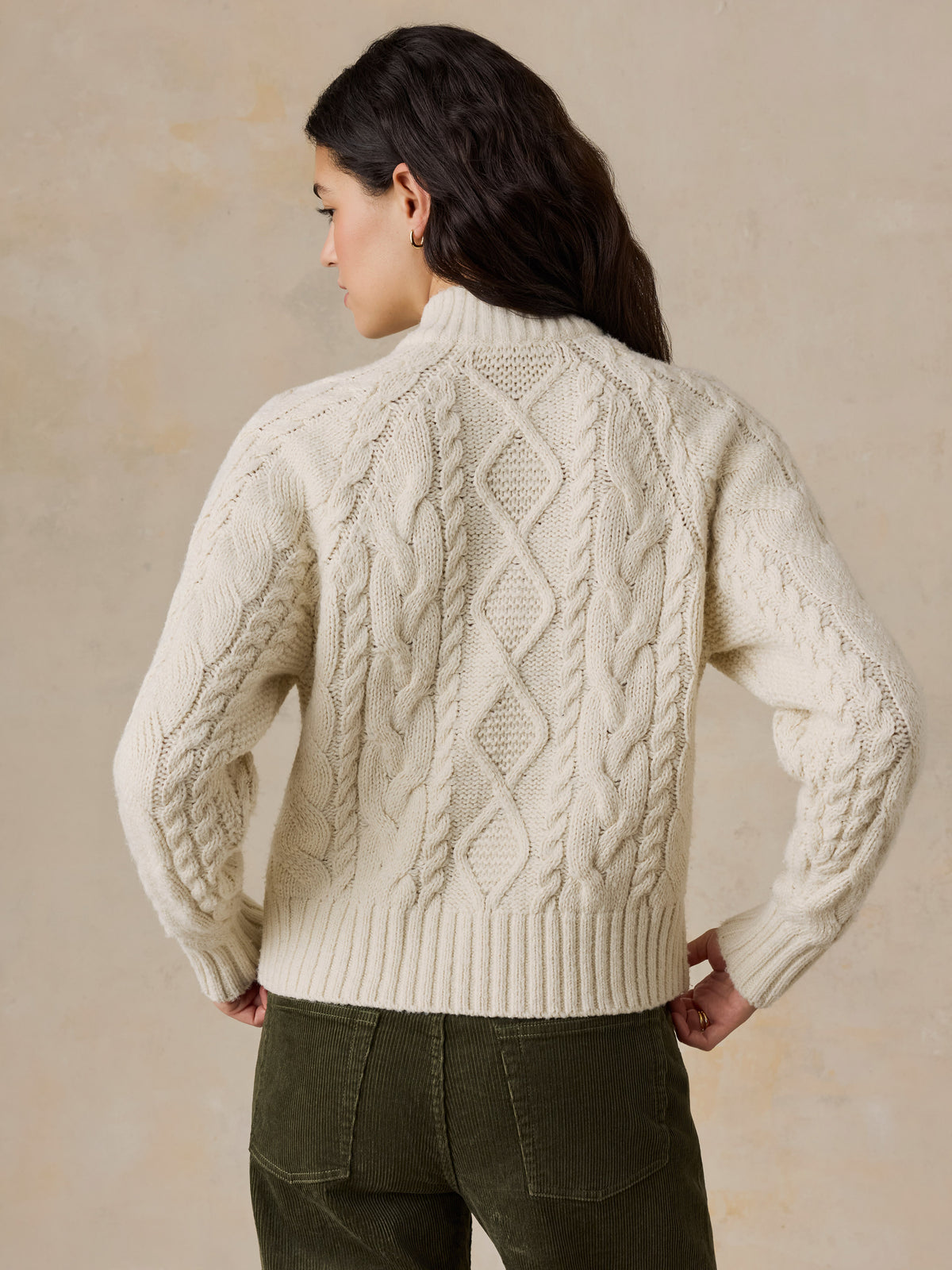 A woman viewed from behind wearing a cream cardigan and green pants, image 4 of 7