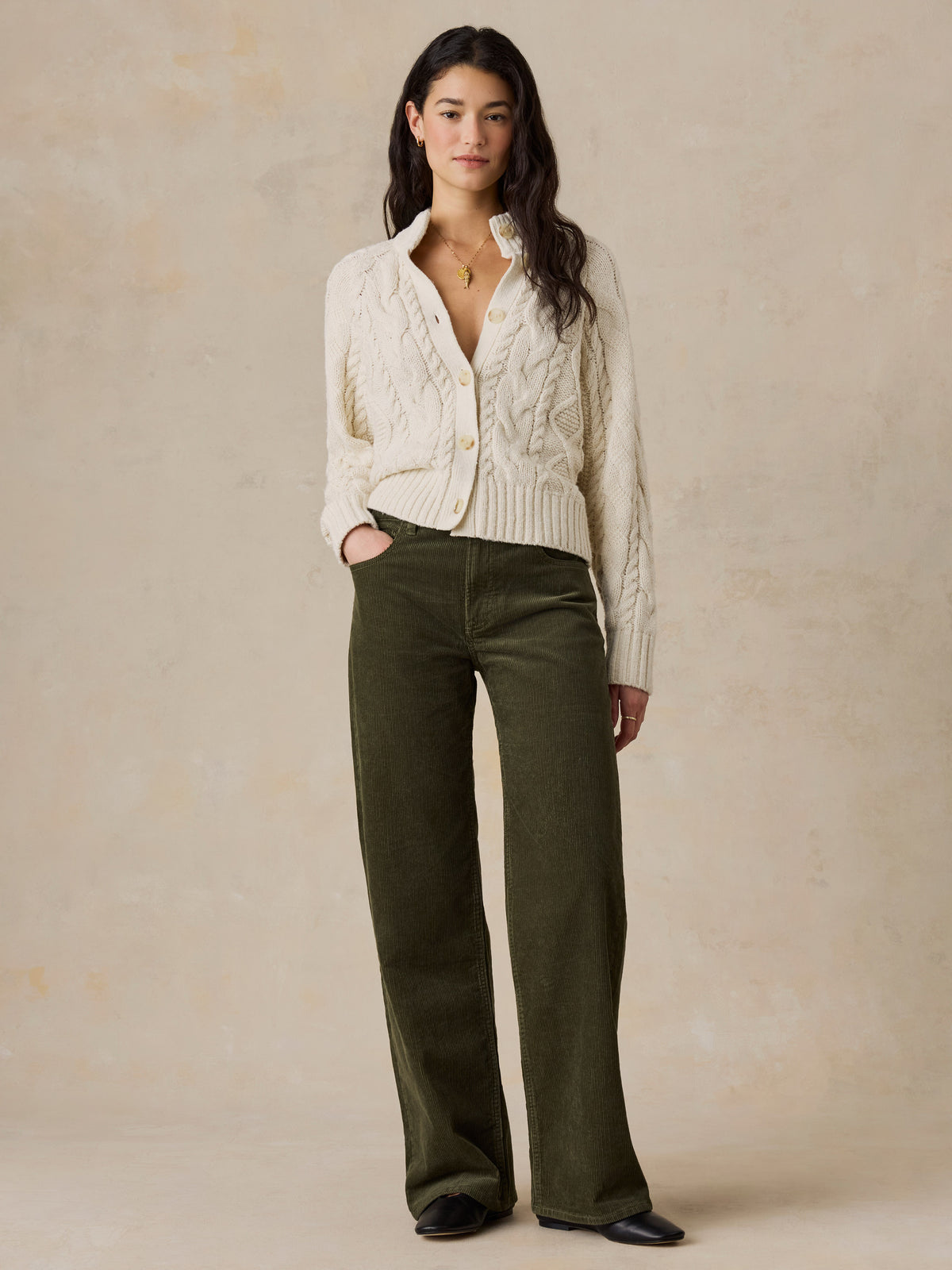 A woman wearing a cream cardigan and green pants, image 3 of 7