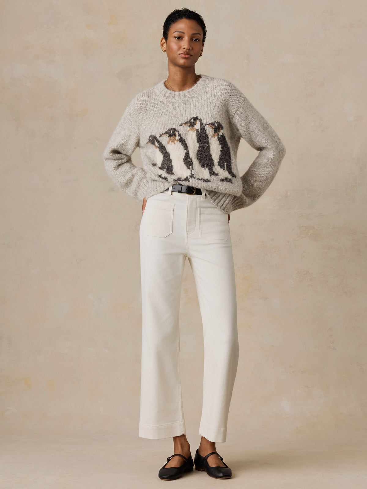 A woman wearing a grey Penguin sweater and white jeans, image 2 of 5