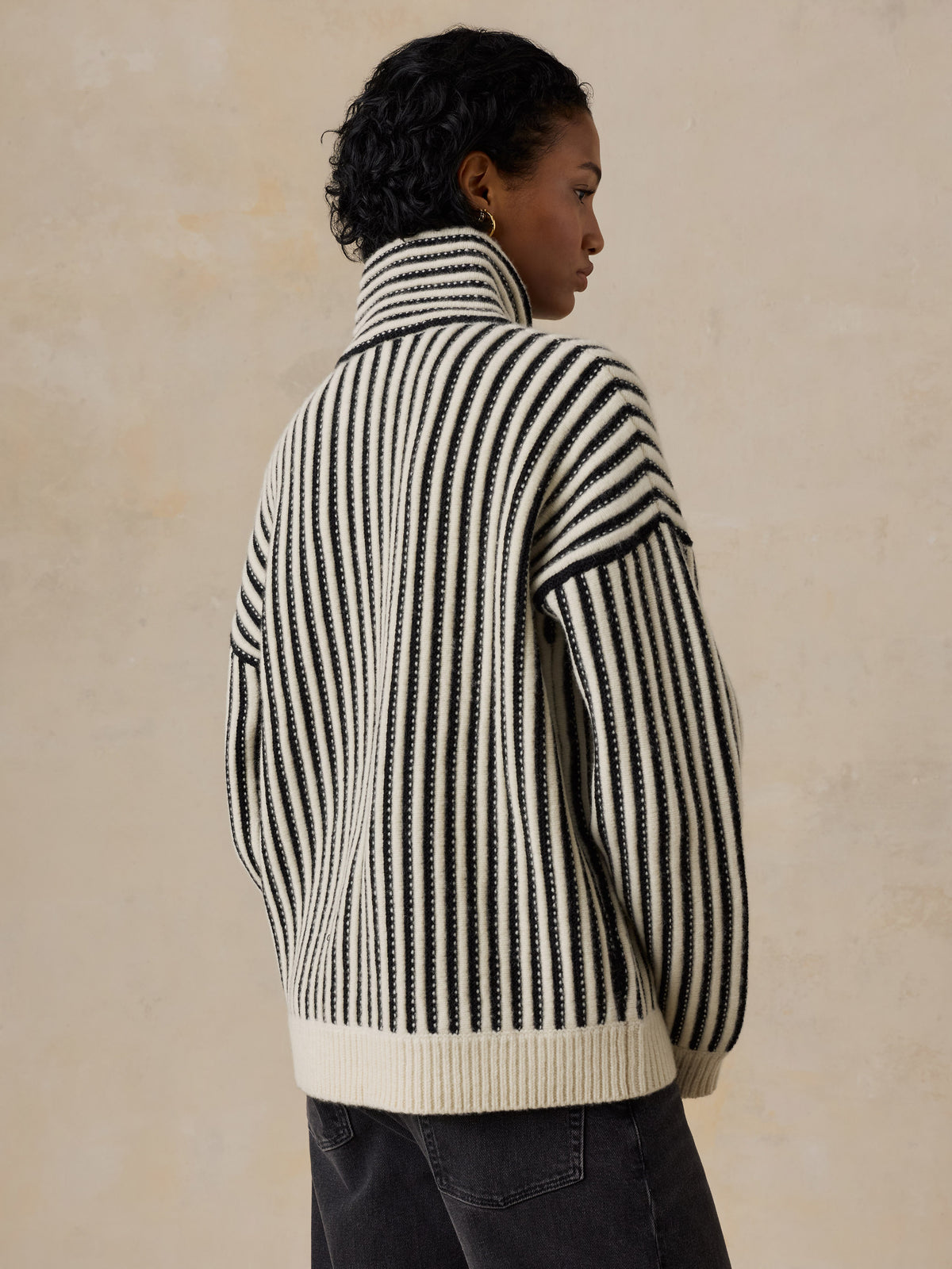 A woman viewed from behind wearing a black and white striped sweater and jeans, image 2 of 5