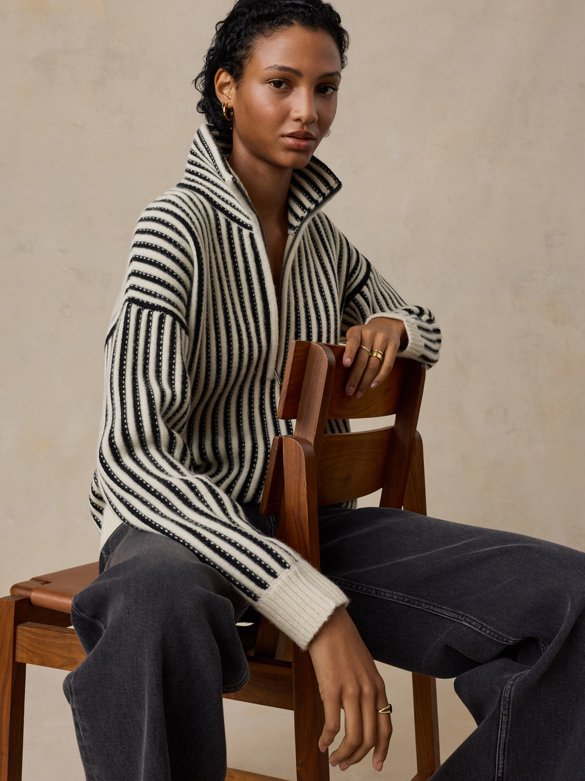 A woman wearing a black and white striped sweater and jeans, image 4 of 5