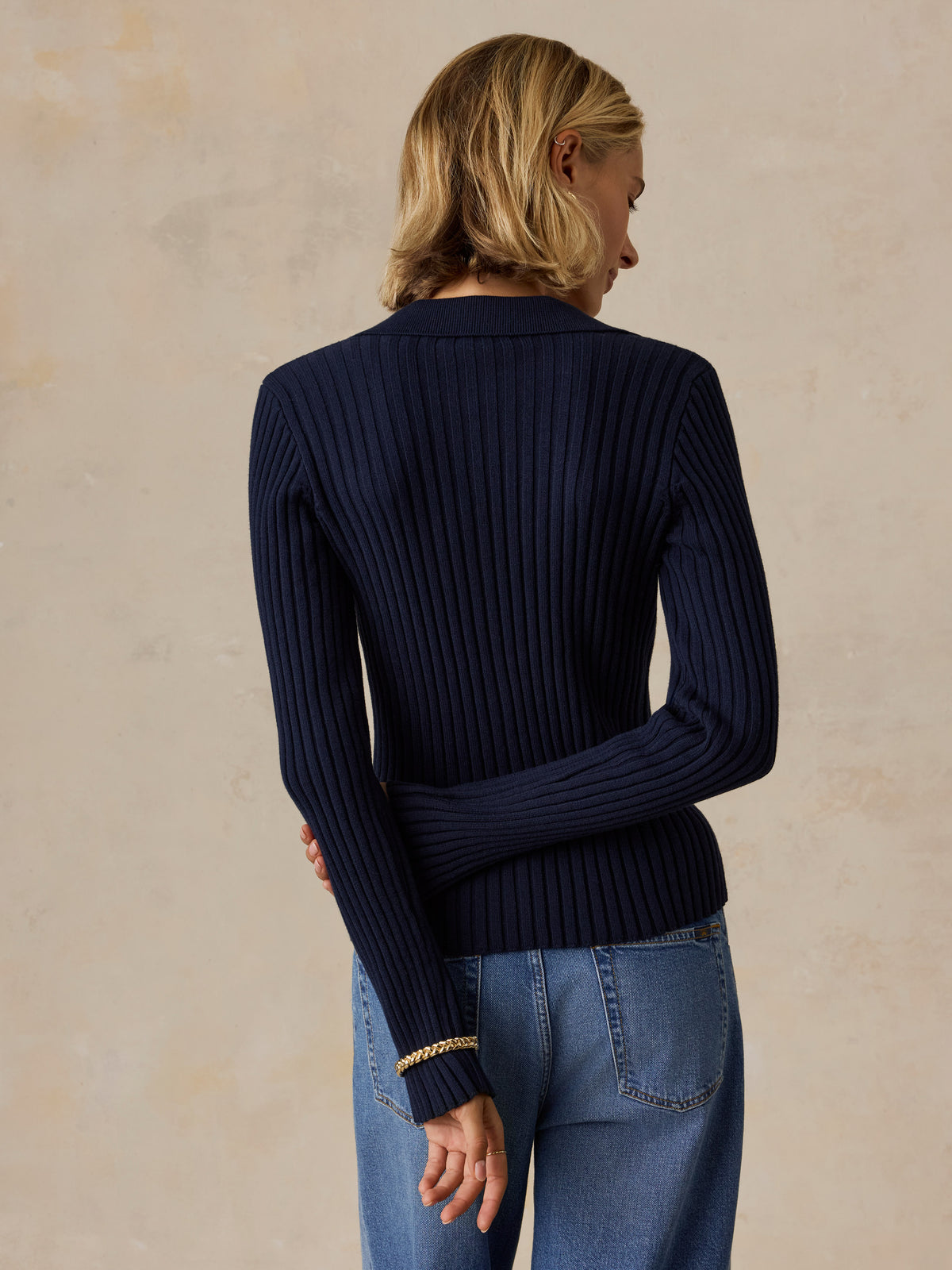 A woman viewed from behind wearing a blue cardigan and jeans, image 2 of 5