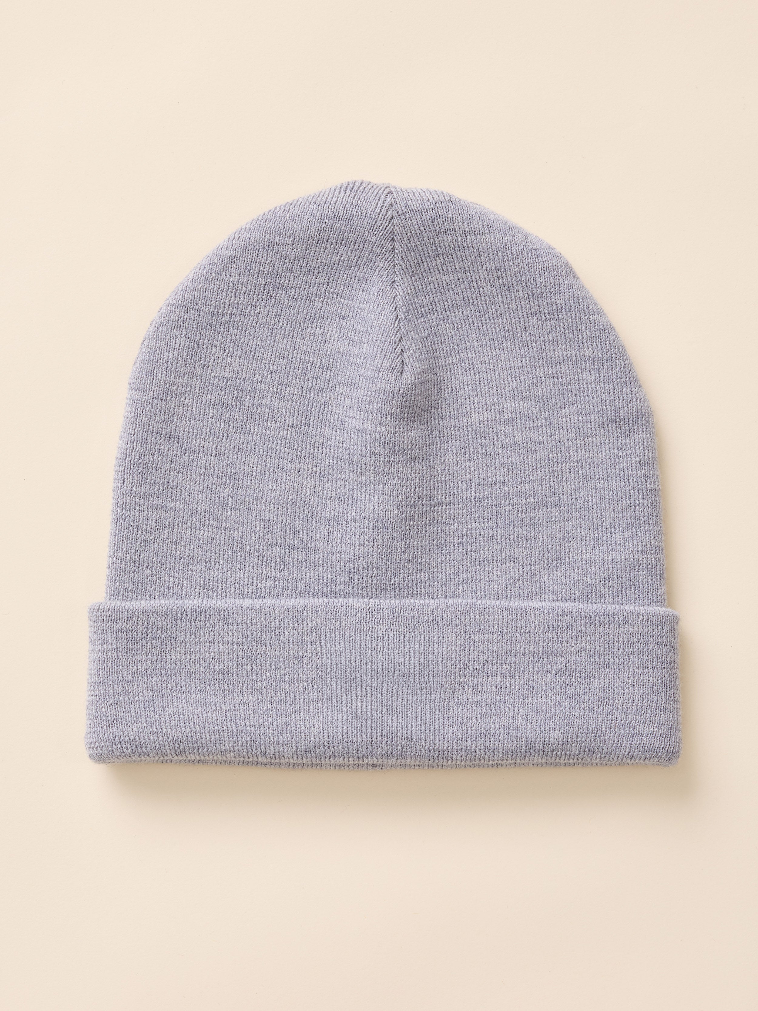 A light gray knit beanie hat with a folded cuff, shown flat against a solid beige background.