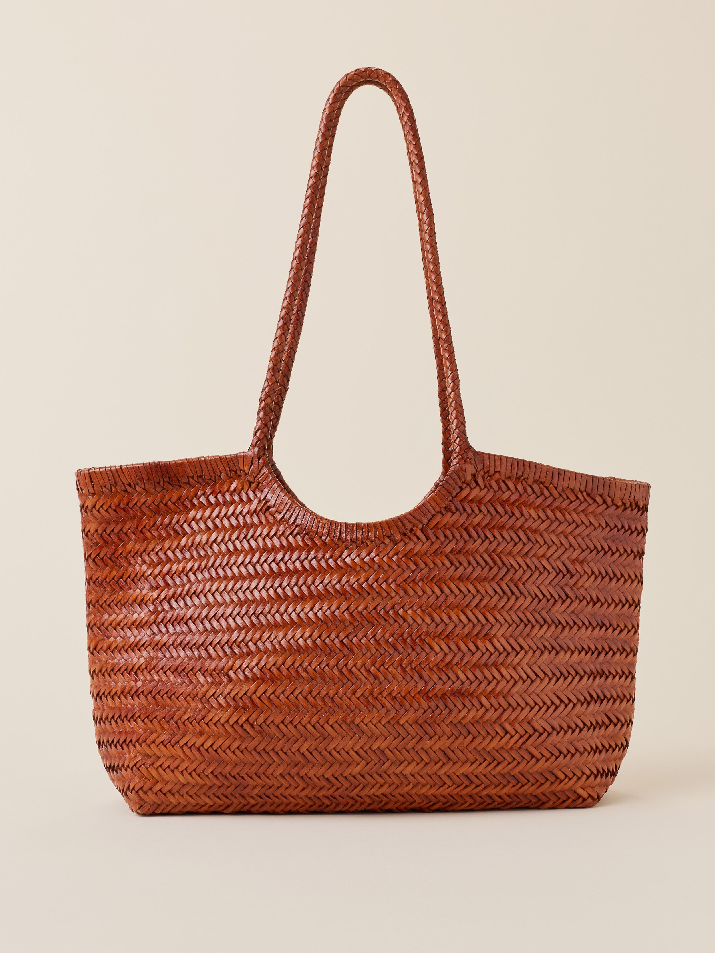A brown woven leather tote bag with a herringbone pattern and two long shoulder straps, shown against a solid light beige background.