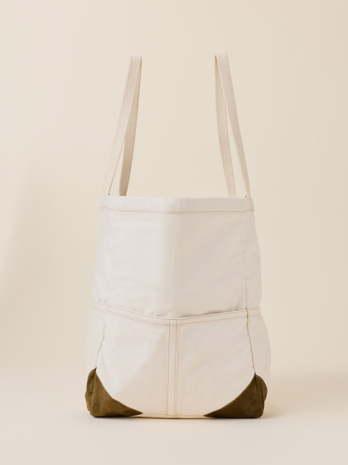 An off-white canvas tote bag with olive green reinforced bottom corners, shown against a solid cream background.