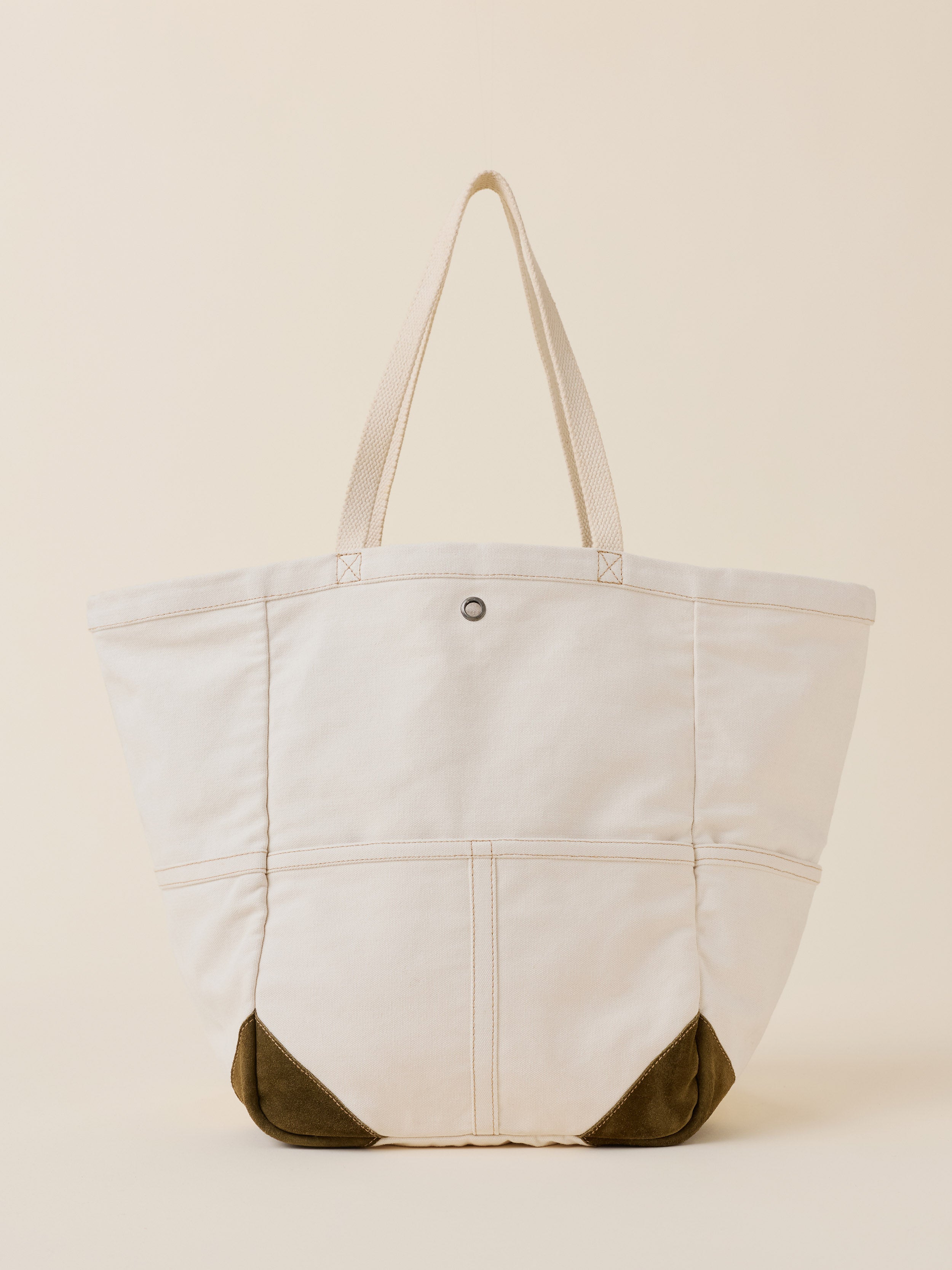 An off-white canvas tote bag with dark olive green suede-like corner protectors and matching shoulder straps, shown against a solid cream background.