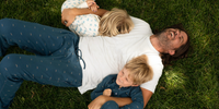 Dad laying on the grass with his two kids in pajamas. 