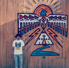 man standing against a native inspired wall mural