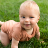 Baby in a onesie on the grass.