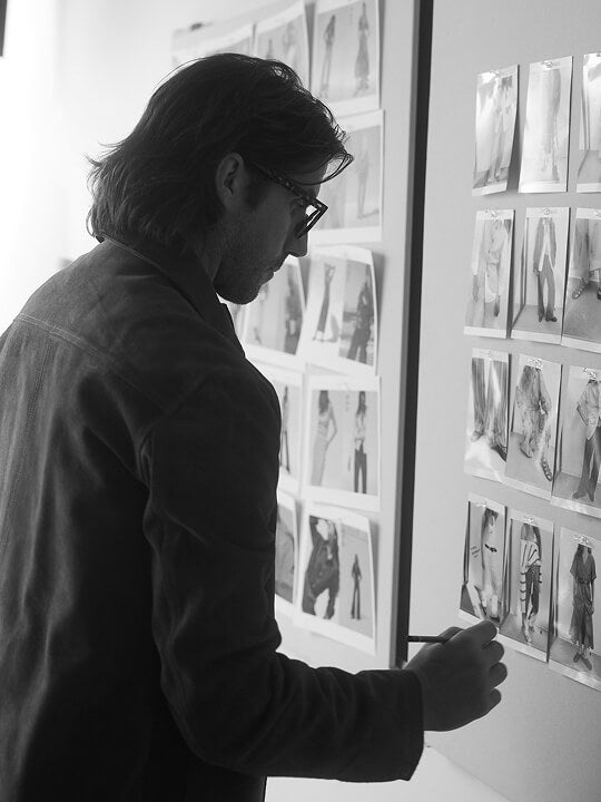 A black and white photo of mike faherty making notes on a wall of images of fit models wearing sample clothing
