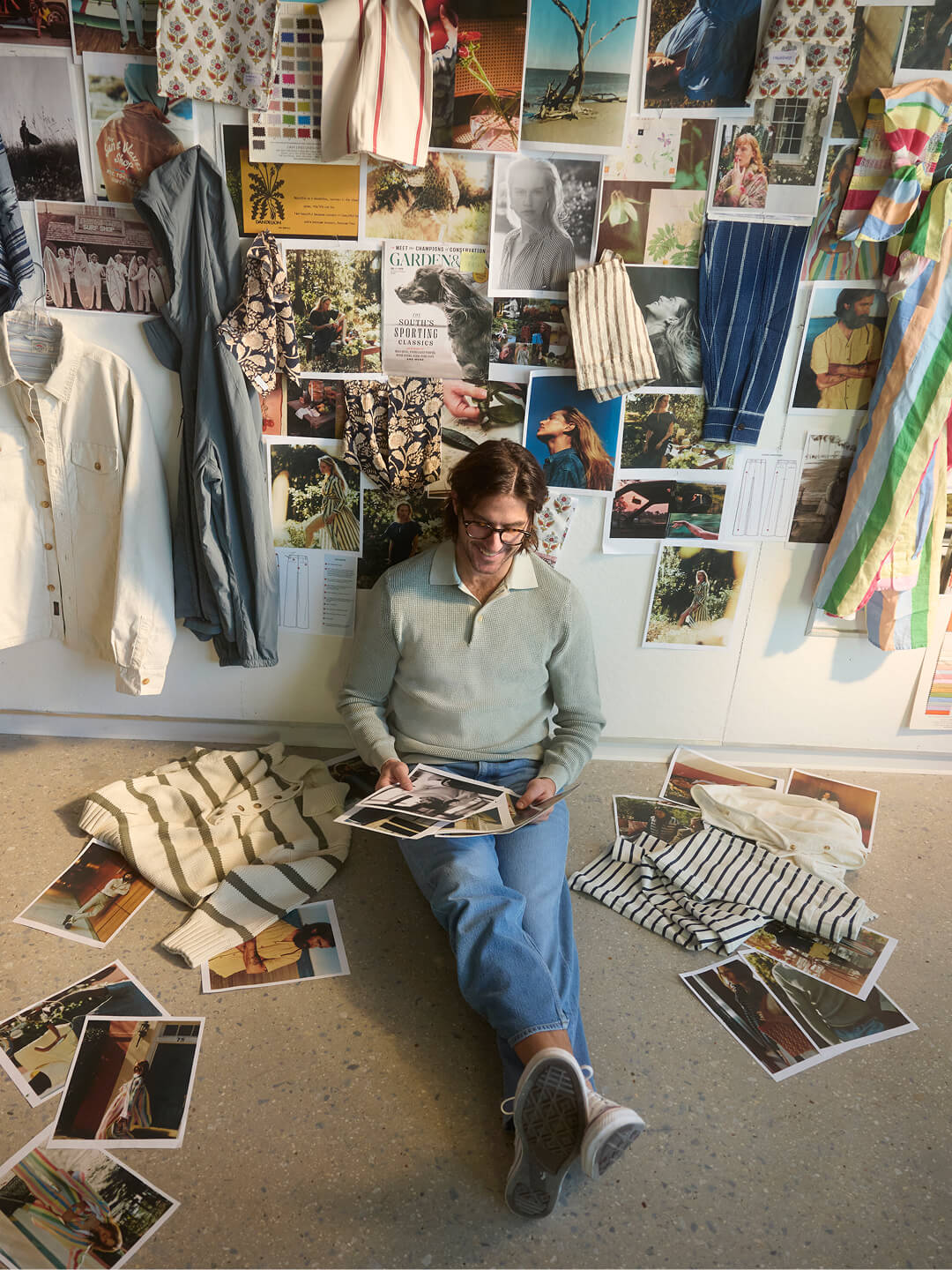 Mike Faherty sits in his design studio in front of a wall covered in inspirational imagery and fabrics. He goes through a pile of swiped imagery as he begins to design his new collection.