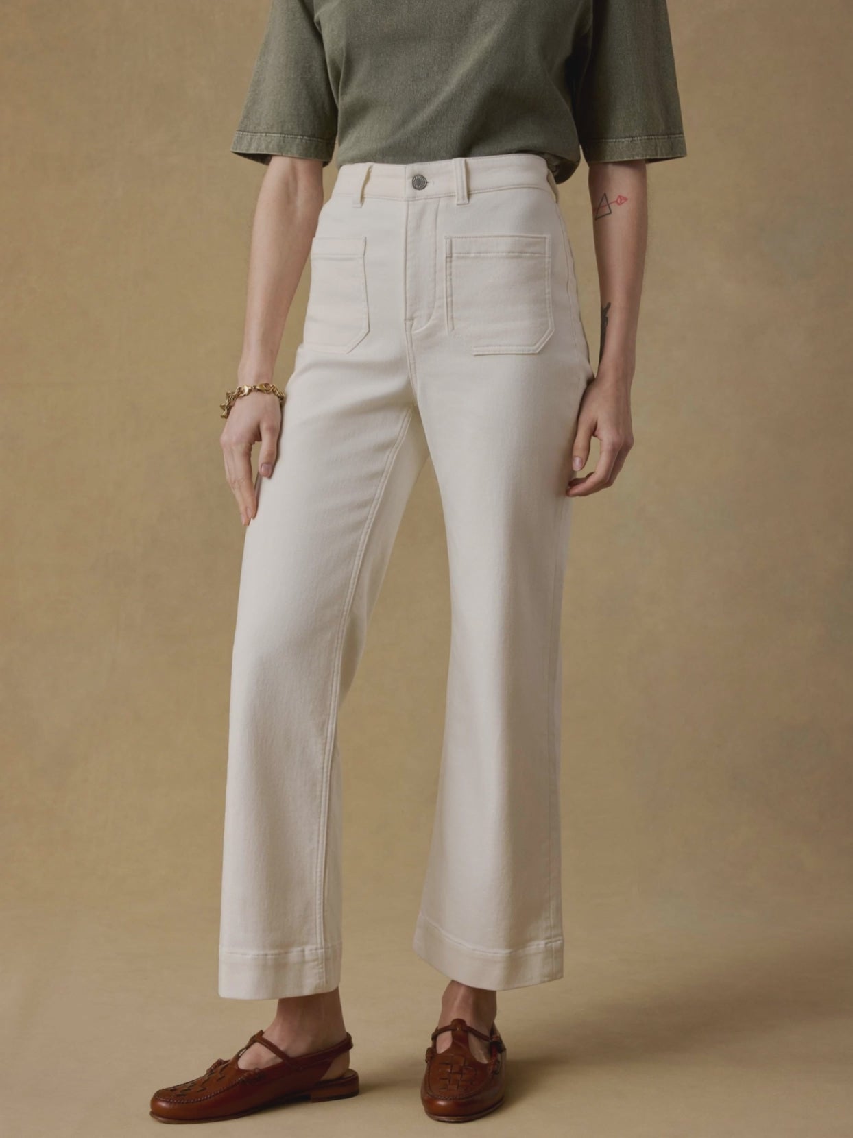Video of a woman wearing white jeans with an olive green t-shirt against a beige background
