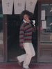 Video of a woman wearing a long-sleeve rugby-style shirt with stripes in olive green, navy blue, red, and mustard yellow and white pants