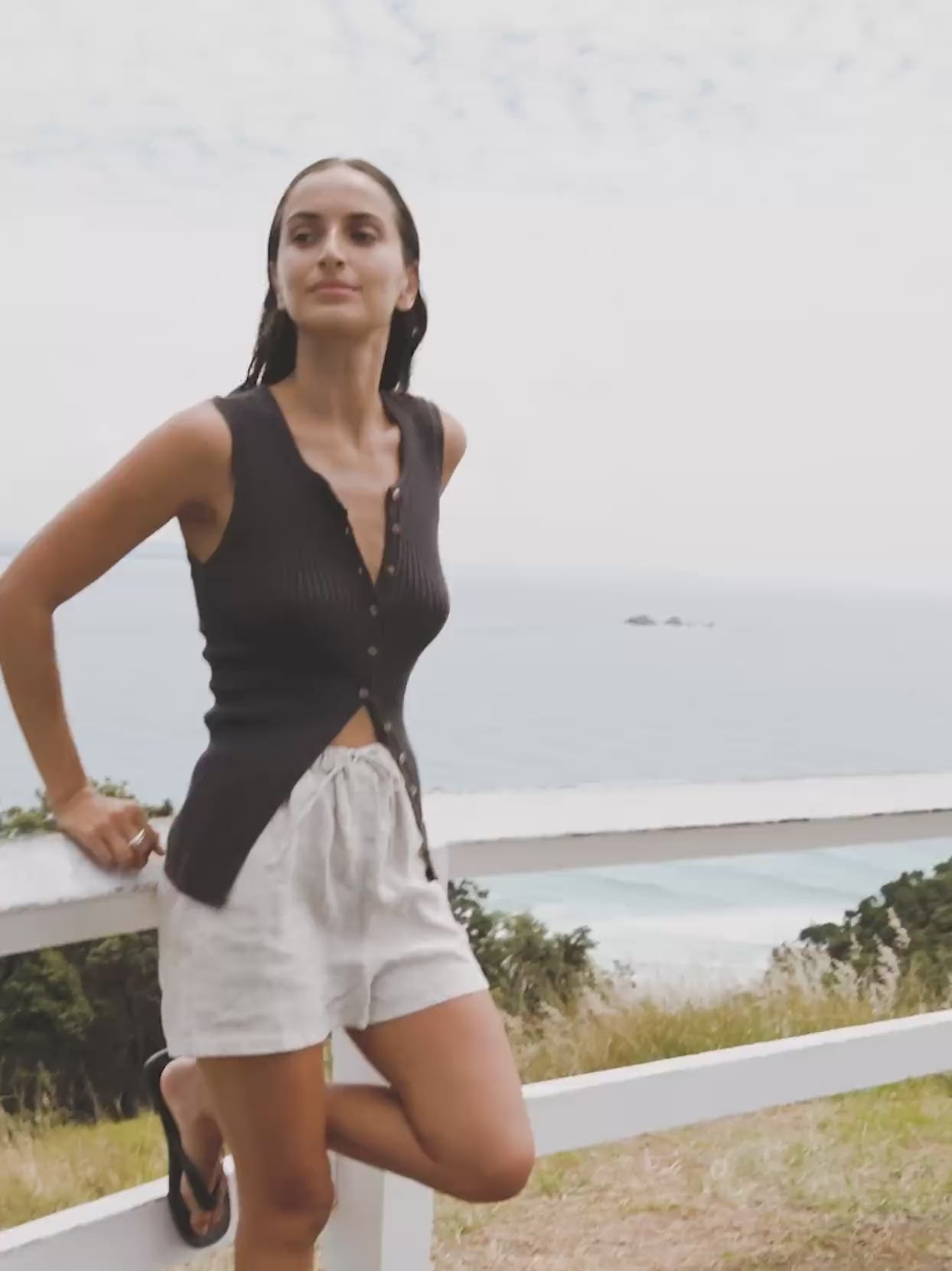 Video of a woman wearing flax shorts and a black tank top overlooking the ocean