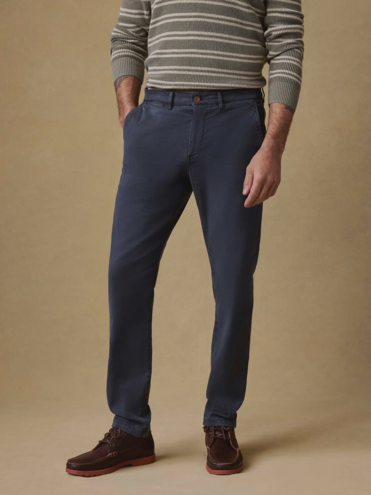Video of a man wearing blue chino pants, a green striped waffle long sleeve tee, and brown boots against a beige background