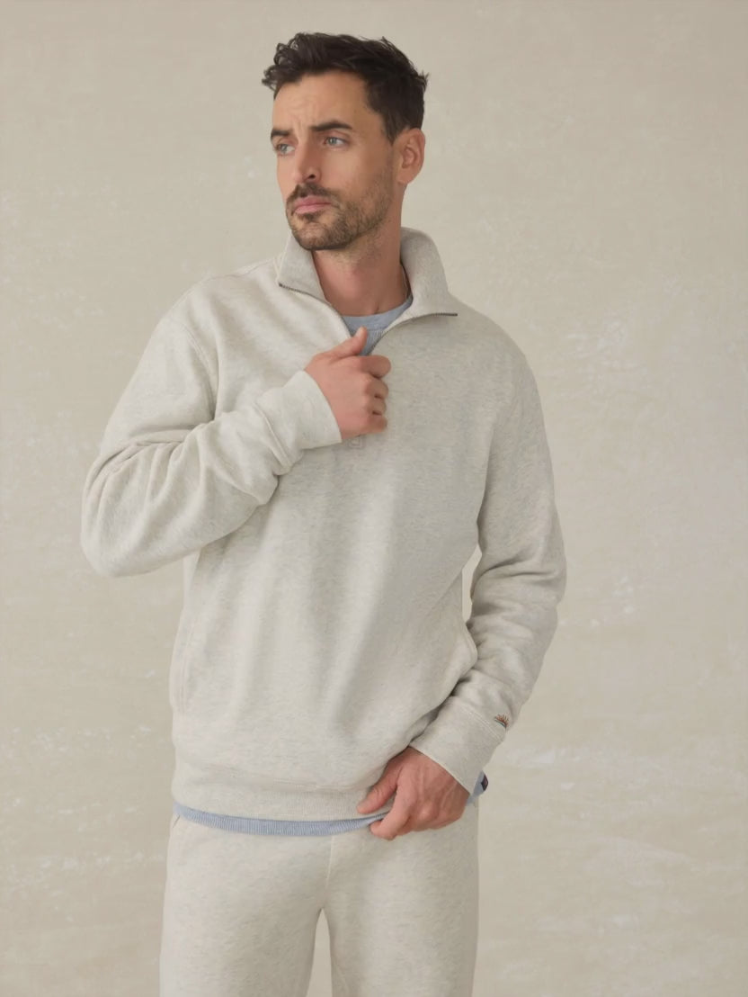 Man wearing a heather grey quarter zip against a beige background