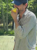 Man eating a piece of fruit wearing a striped shirt with a blue hat walking outside in nature