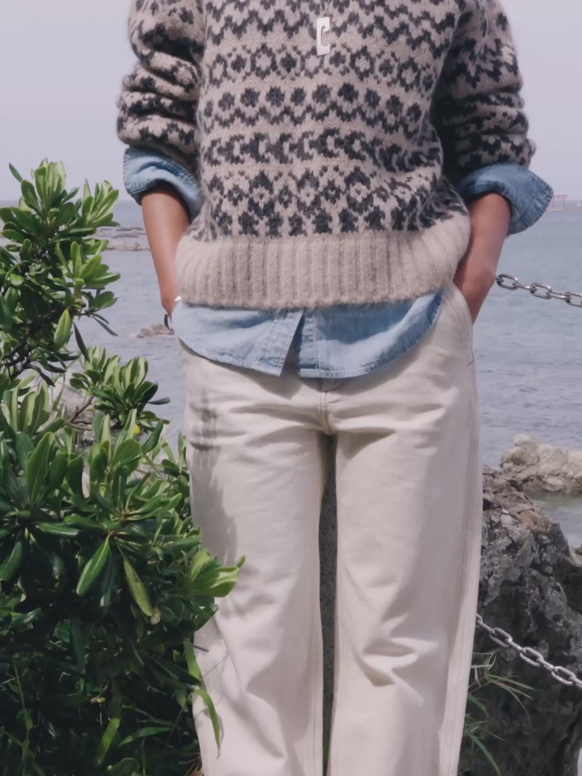Video of a woman wearing a beige and black fairisle sweater over a chambray shirt and white pants