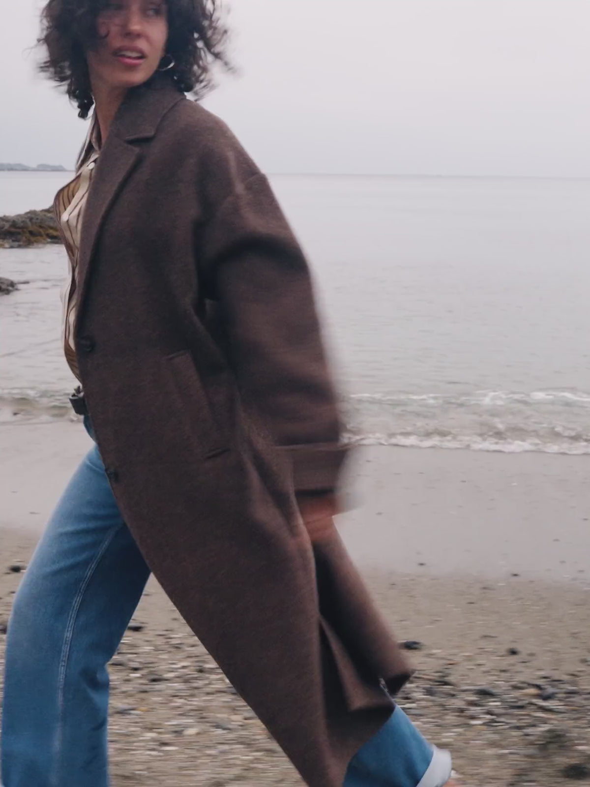 Video of a woman wearing a brown coat over a striped shirt and blue jeans