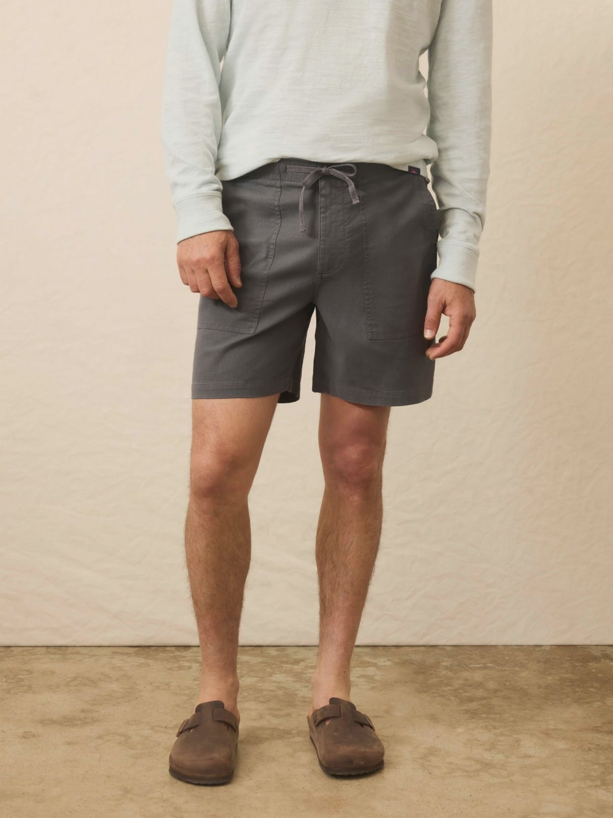 Video of a man wearing black shorts with a light blue henley against a beige background