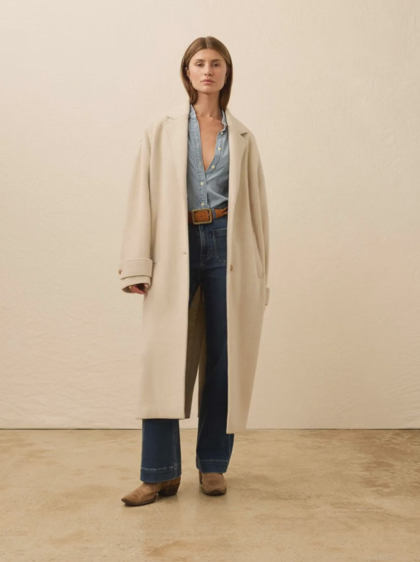 Woman wearing a beige coat over a blue shirt against a beige background