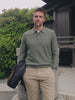 Video of a man wearing a green long sleeve sweater polo and chino pants standing outside a japanese house holding a jacket