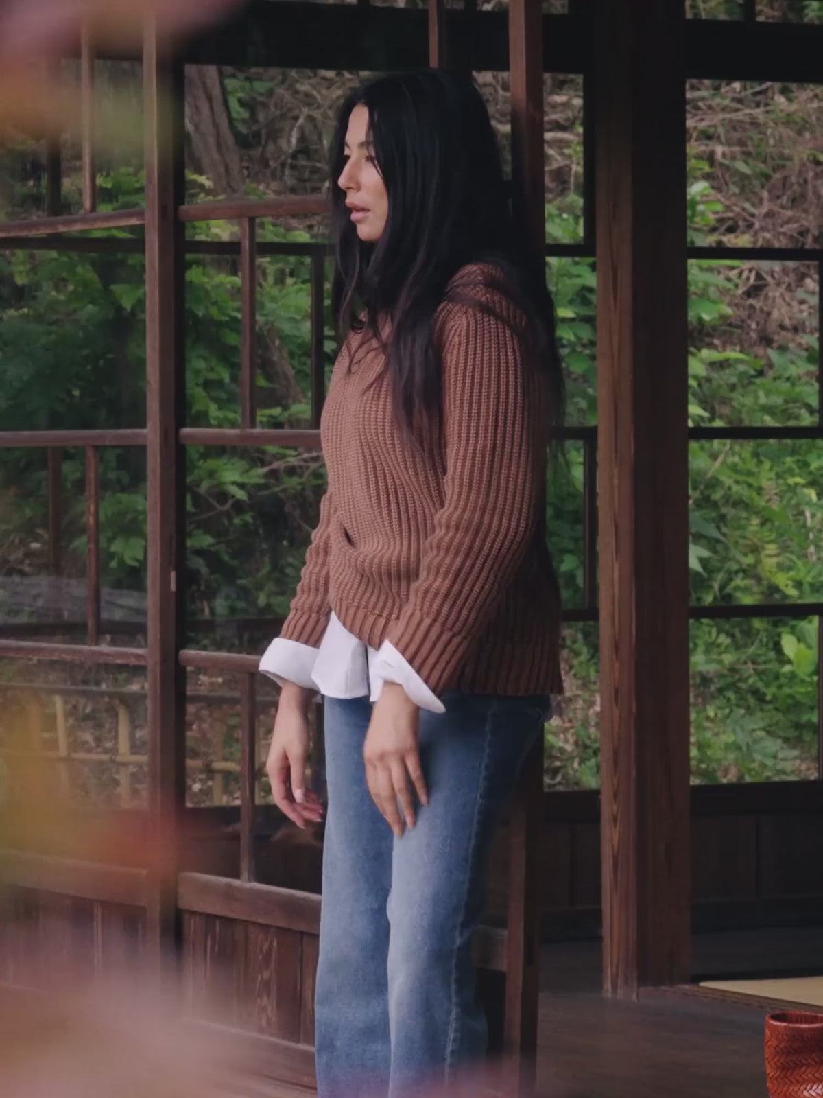 Video of a woman wearing a brown sweater over a white poplin shirt and blue jeans