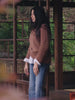 Video of a woman wearing a brown sweater over a white poplin shirt and blue jeans