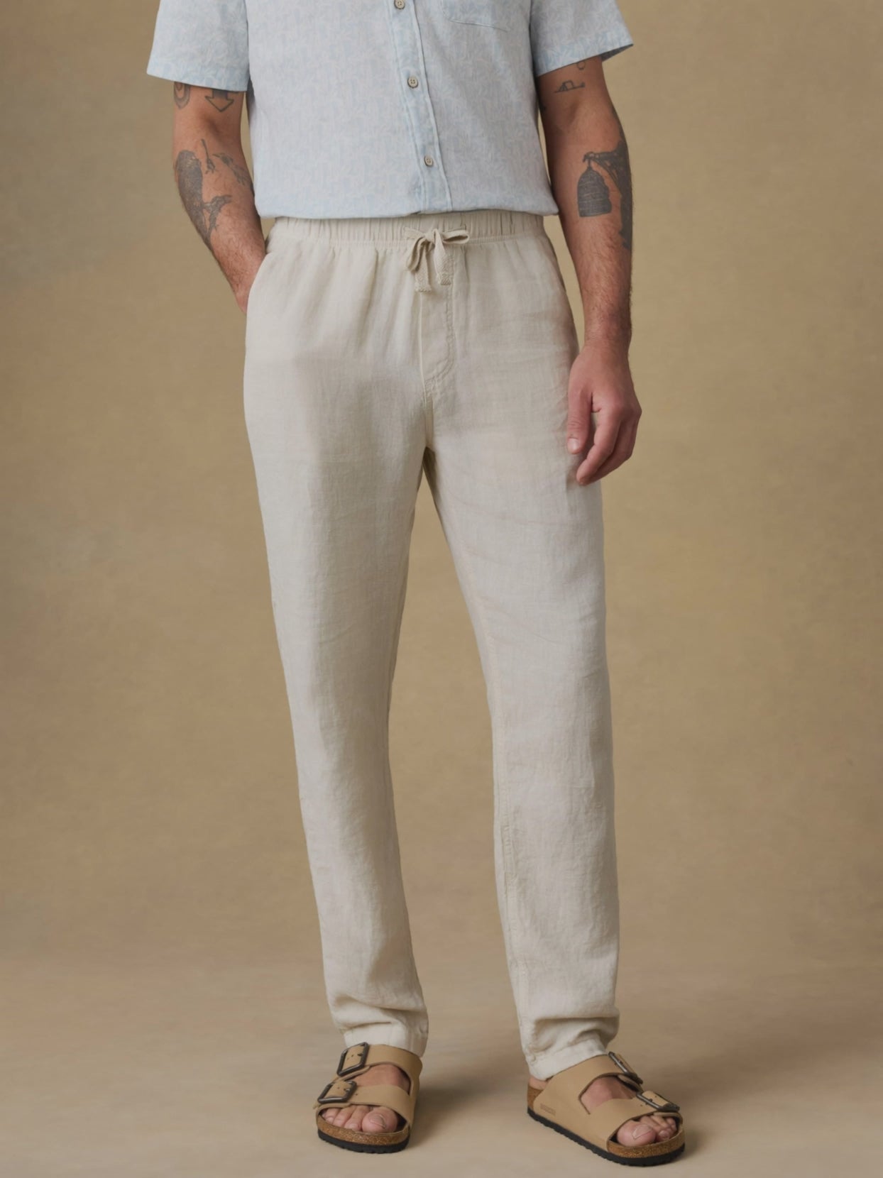 Video of a man wearing a light blue linen shirt with beige linen pants against a beige background