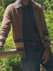 Man wearing a brown zip cardigan over a blue shirt with blue jeans standing outside in nature