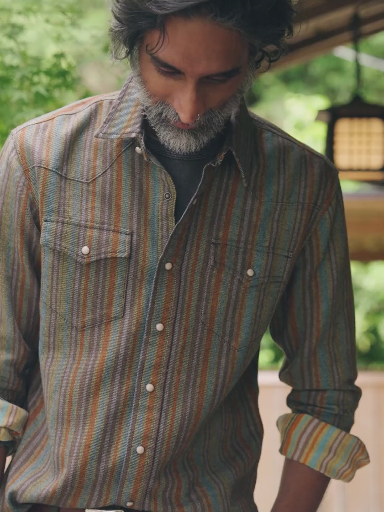Man wearing a colorful striped button down western style shirt standing outside