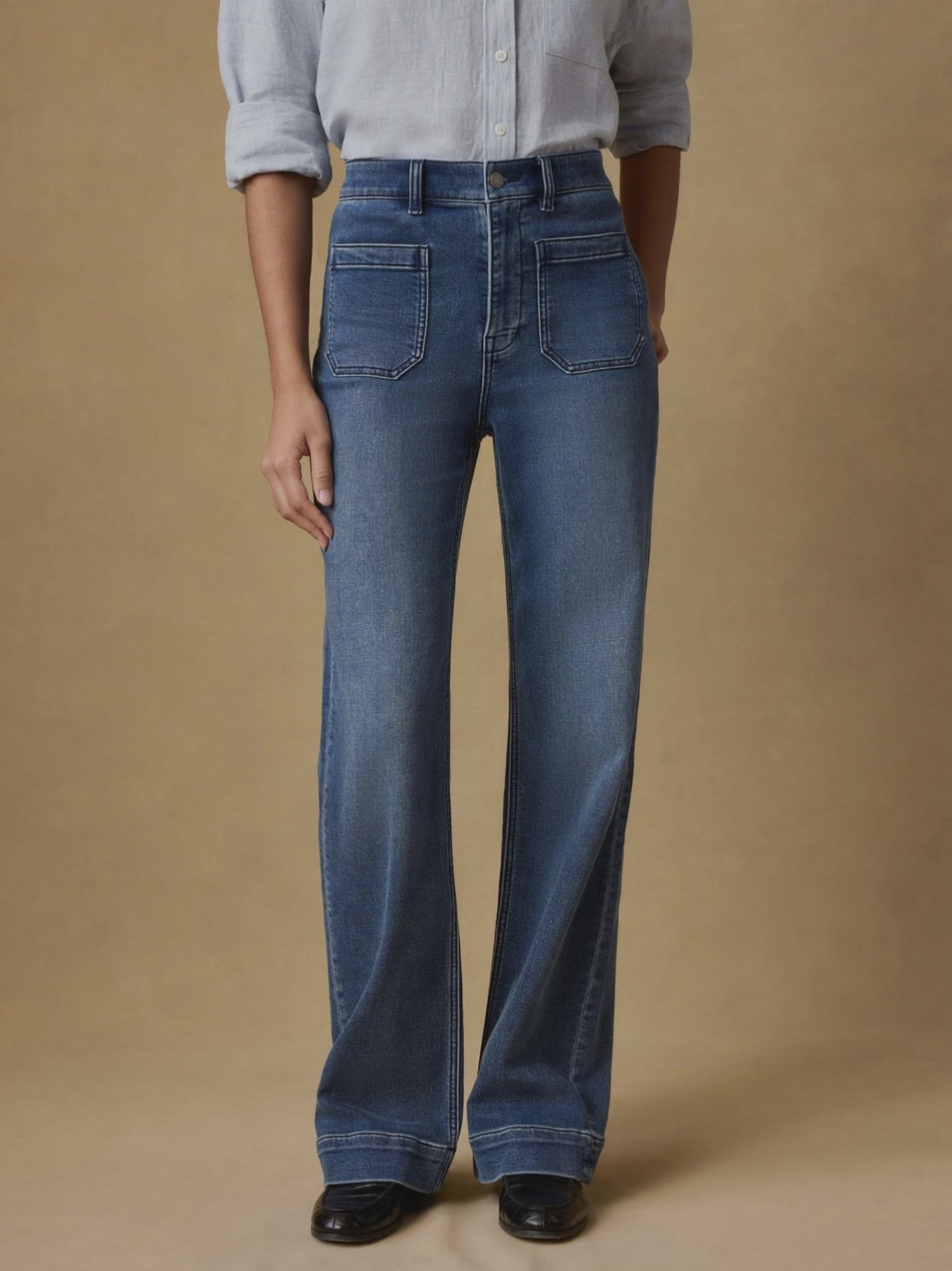 Video of a woman wearing blue stretch terry pants and a light blue linen shirt against a beige background