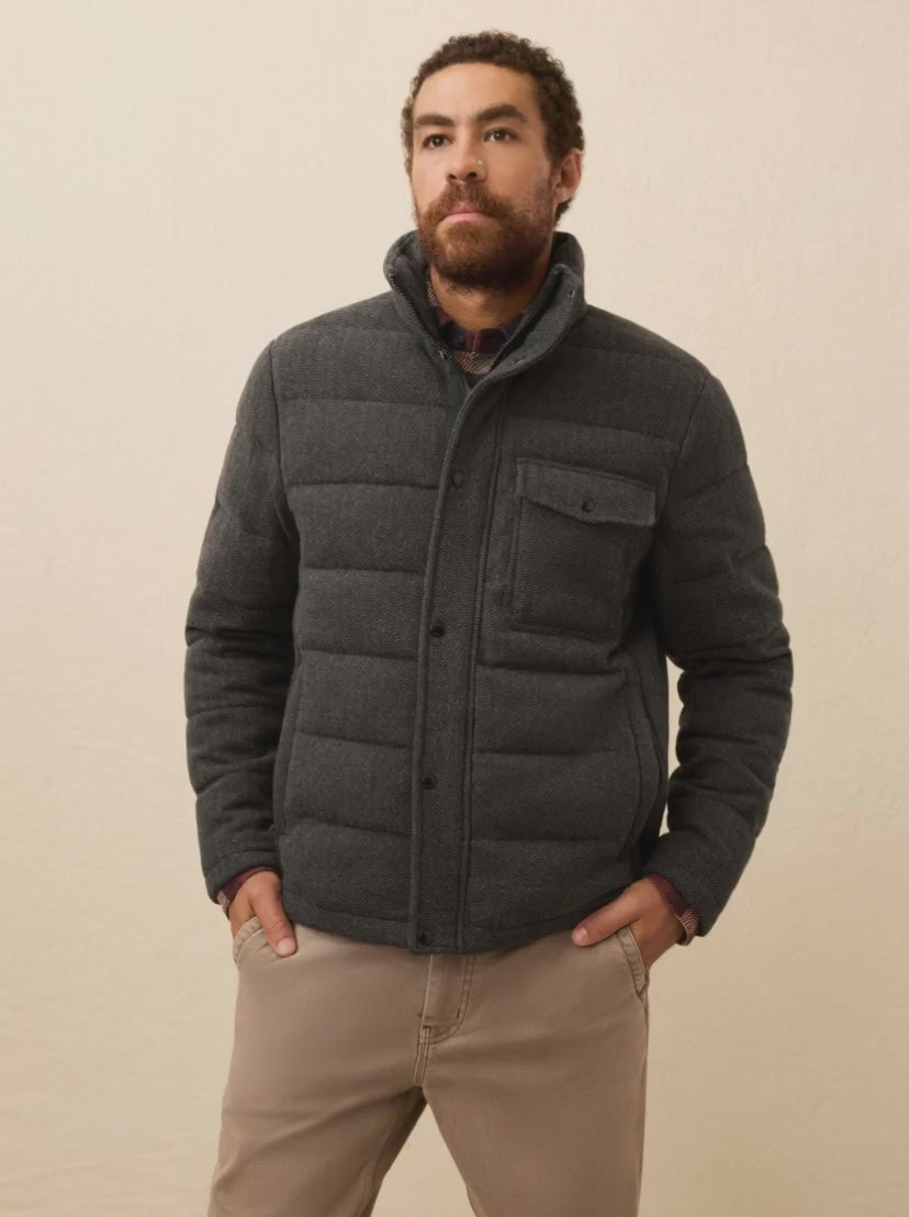 Man is wearing a dark grey quilted jacket against a beige background