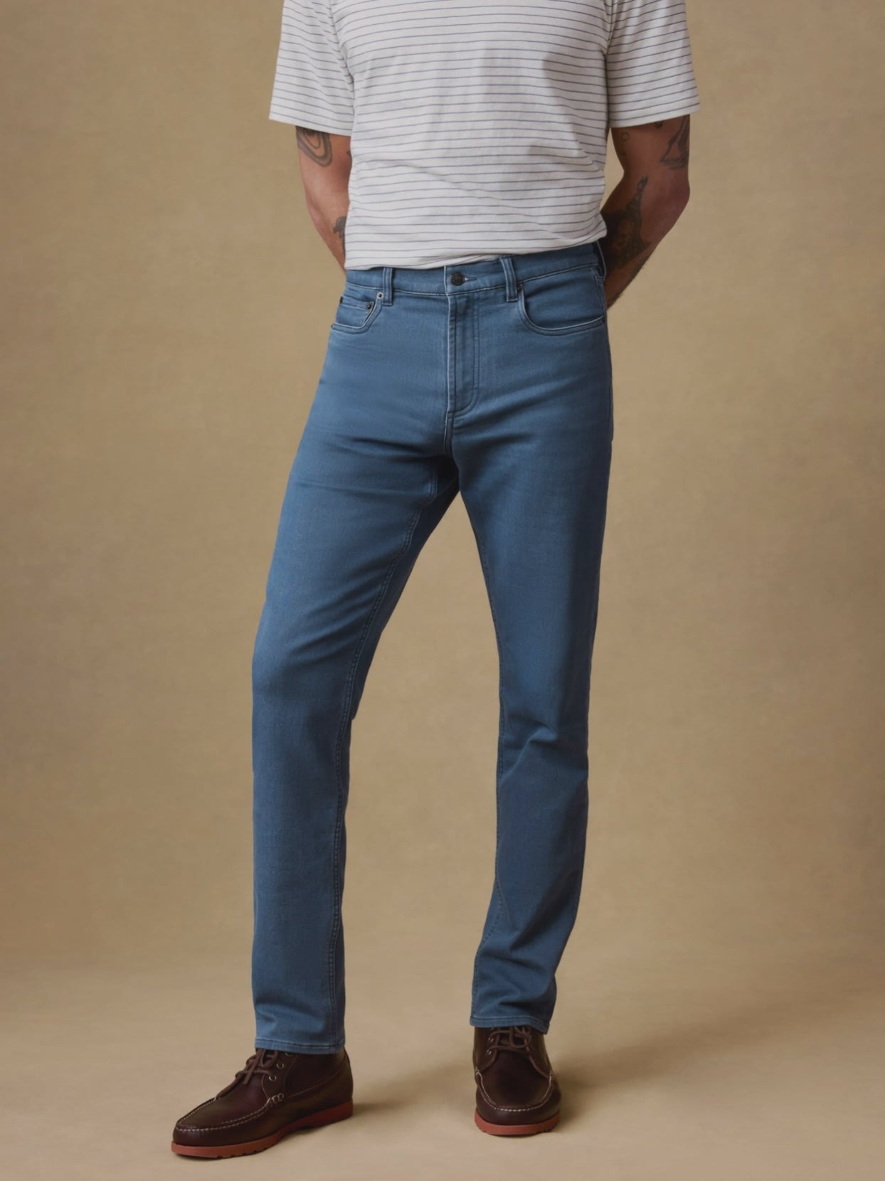 Video of a man wearing a striped t-shirt and blue jeans against a beige background