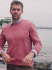 Video of a man wearing a red shirt over a blue button down shirt standing near the sea