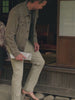 Man wearing chino pants and a twill jacket over a striped t-shirt sitting outside a japanese house